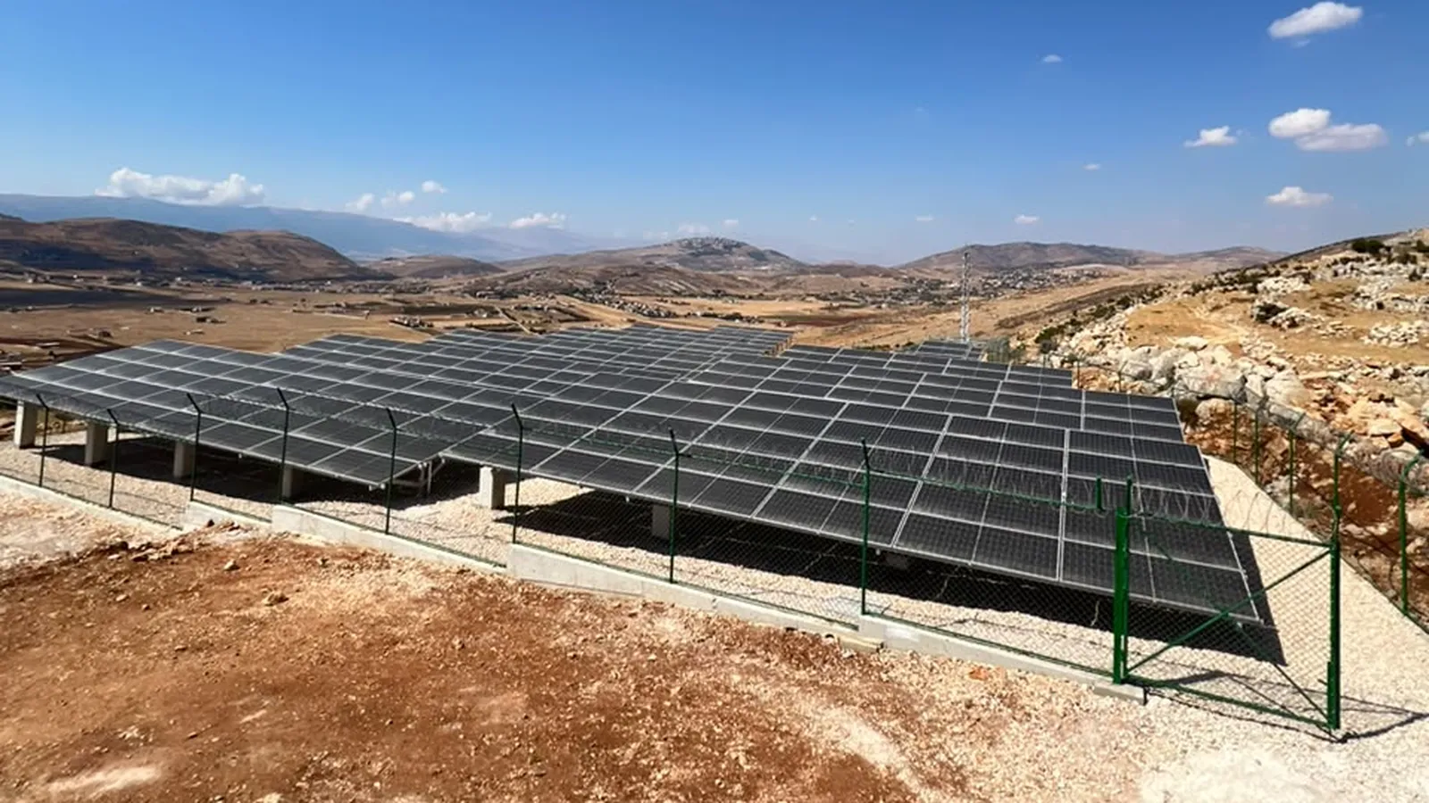 The completed solar plant on a Bekaa hillside — rows of panels on concrete plinths inside a perimeter fence, with the valley and mountains behind.