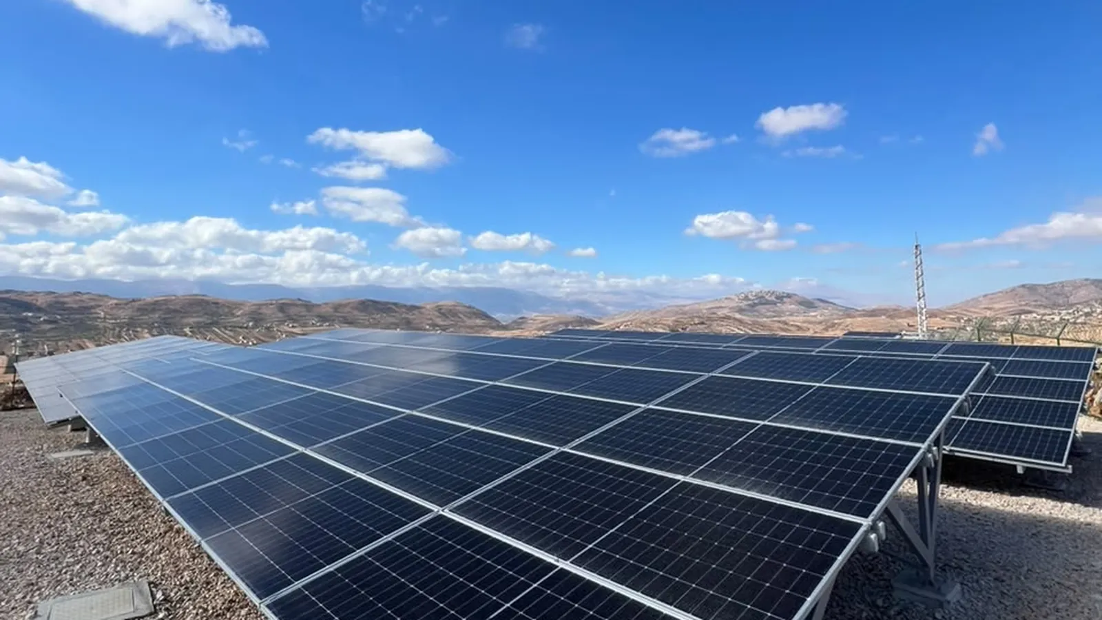 The finished array from ground level: panels carried on galvanised steel tables over a gravel bed, with the Bekaa hills beyond.